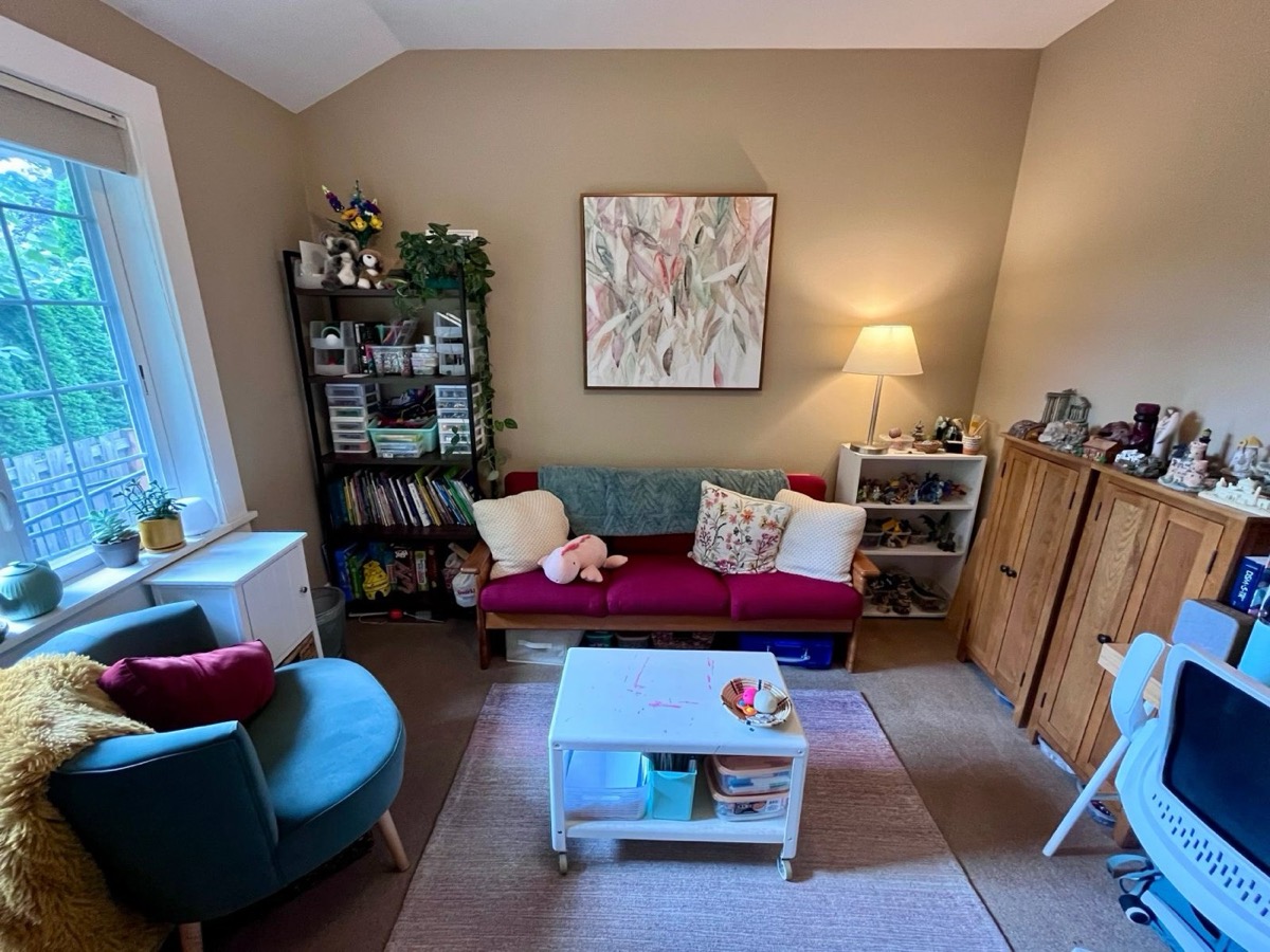 Therapy room with a sofa, armchair, bookshelves, and a play table