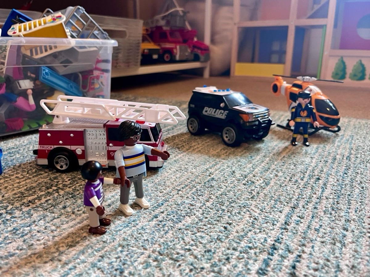 Toy figures, a fire truck, and a police car set up on a playroom rug