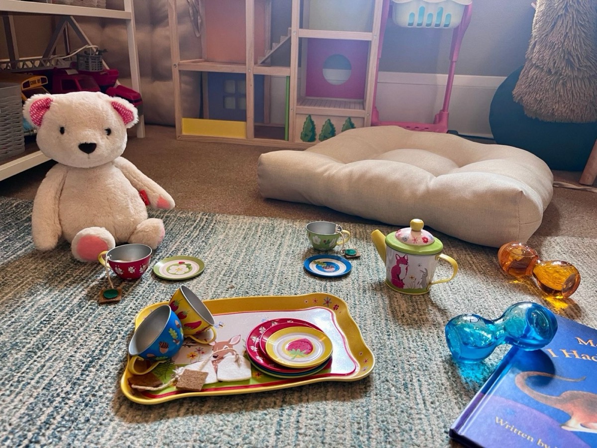 A teddy bear and toy tea set on a playroom rug